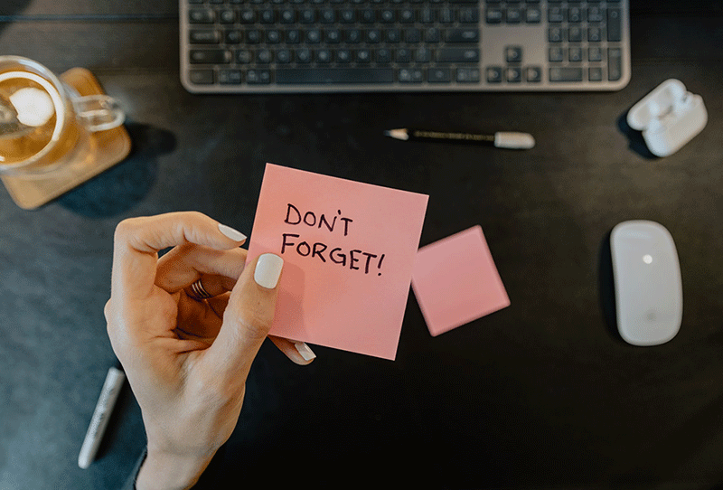 don't forget written on a pink postit note and held over a black desk
